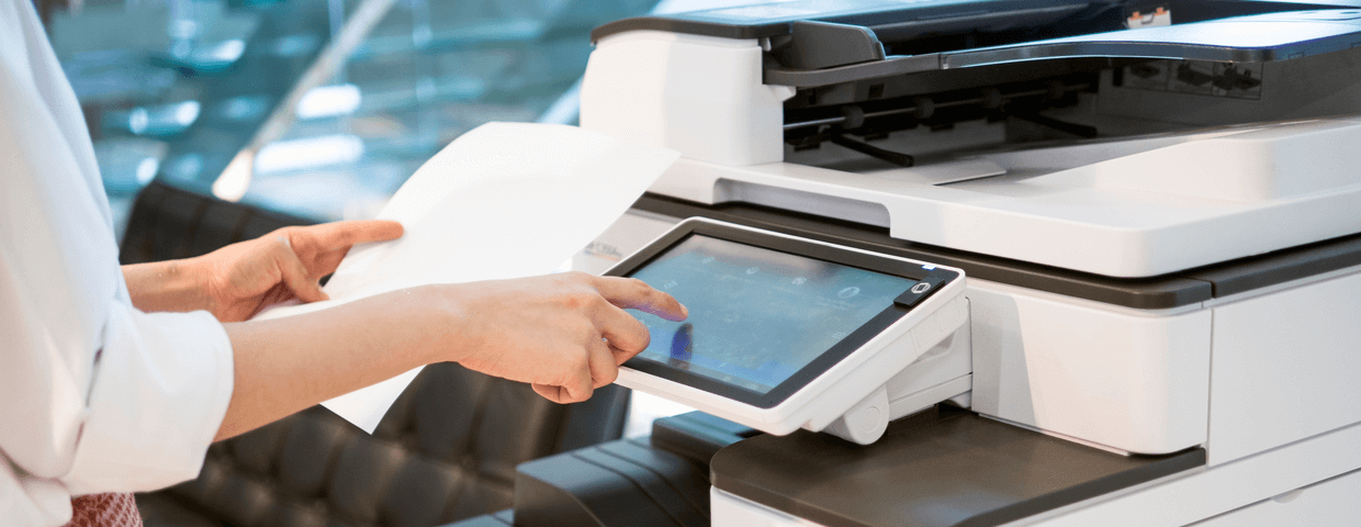 woman standing in front of an office copier or multifunction machine holding a piece of paper ready to make a copy