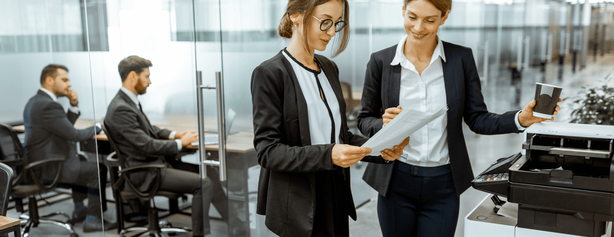 two business woman standing at a copier in an office hallway, copier leasing concept for any company