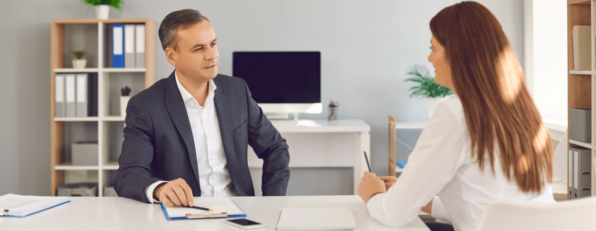 Male and female sitting at a desk in an office having an interview 