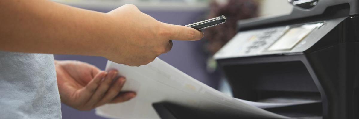 hand holding mobile phone next to printer that has printed a sheet of paper