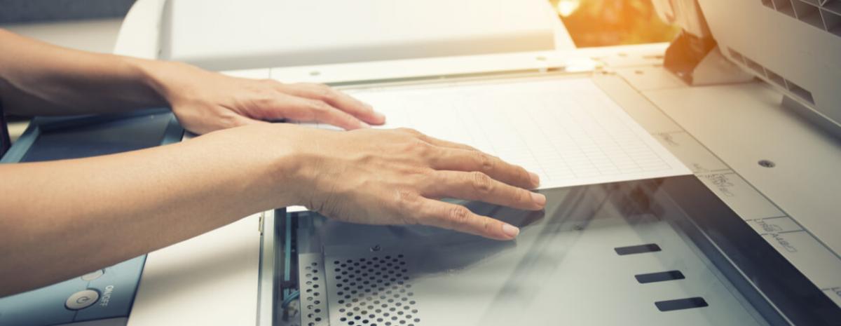 Closeup image of a womans hands putting a sheet of paper into a copying device